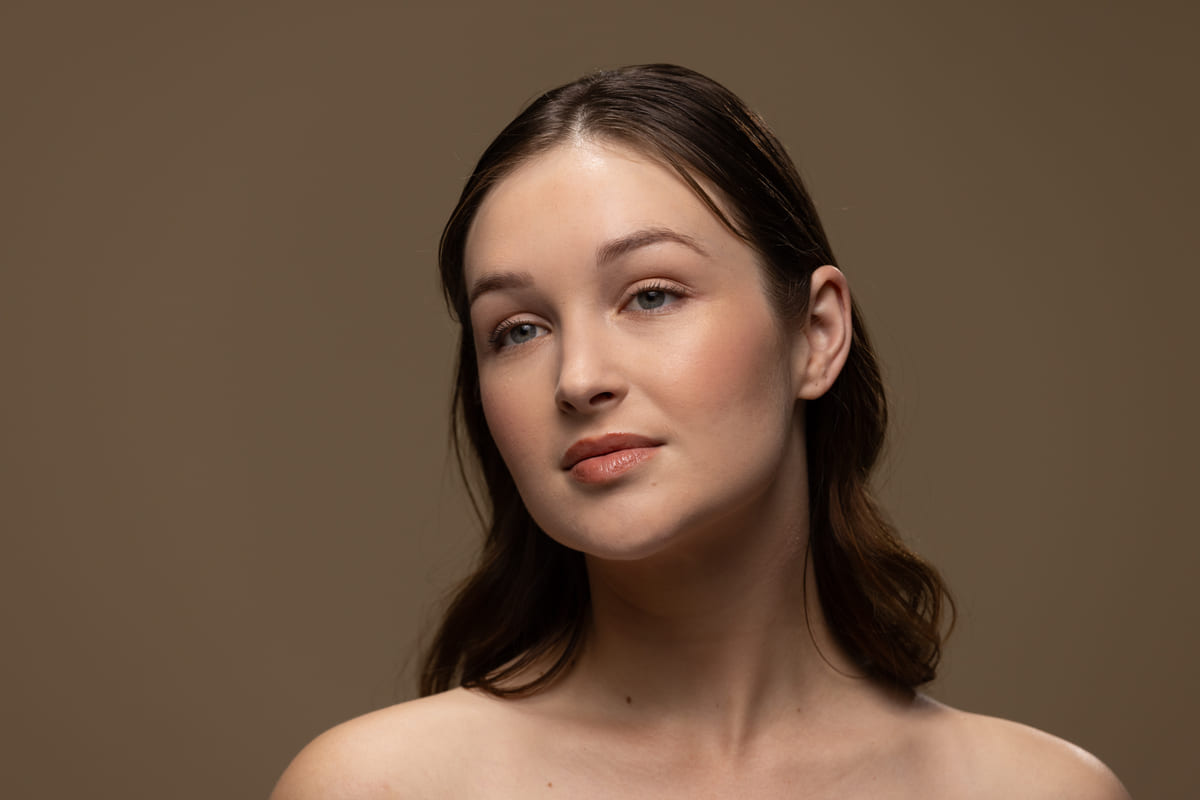 A woman with natural makeup, photographed against a warm neutral background