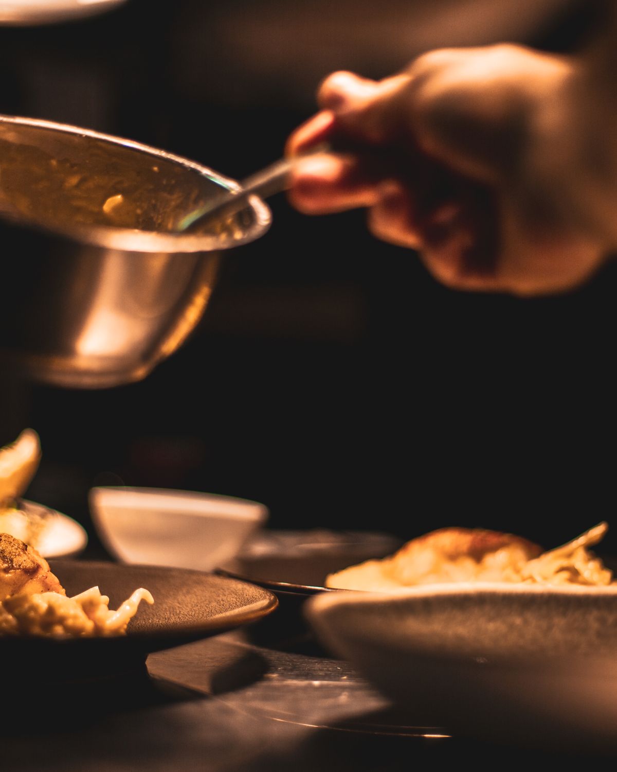 Hands finishing plates on the pass in a low-lit kitchen
