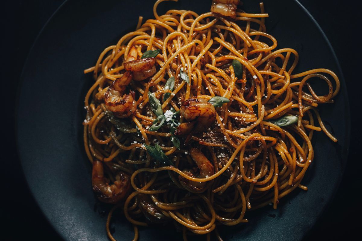 A plate of spaghetti with prawns, shot on a dark table