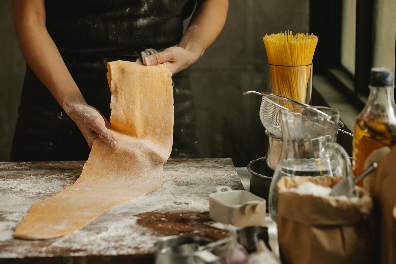 A cook lifting a sheet of fresh egg pasta from a floured bench