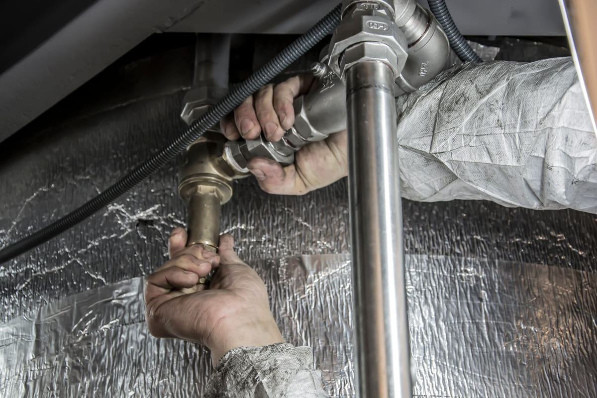 A plumber's hands tightening a fitting on a supply line under a sink
