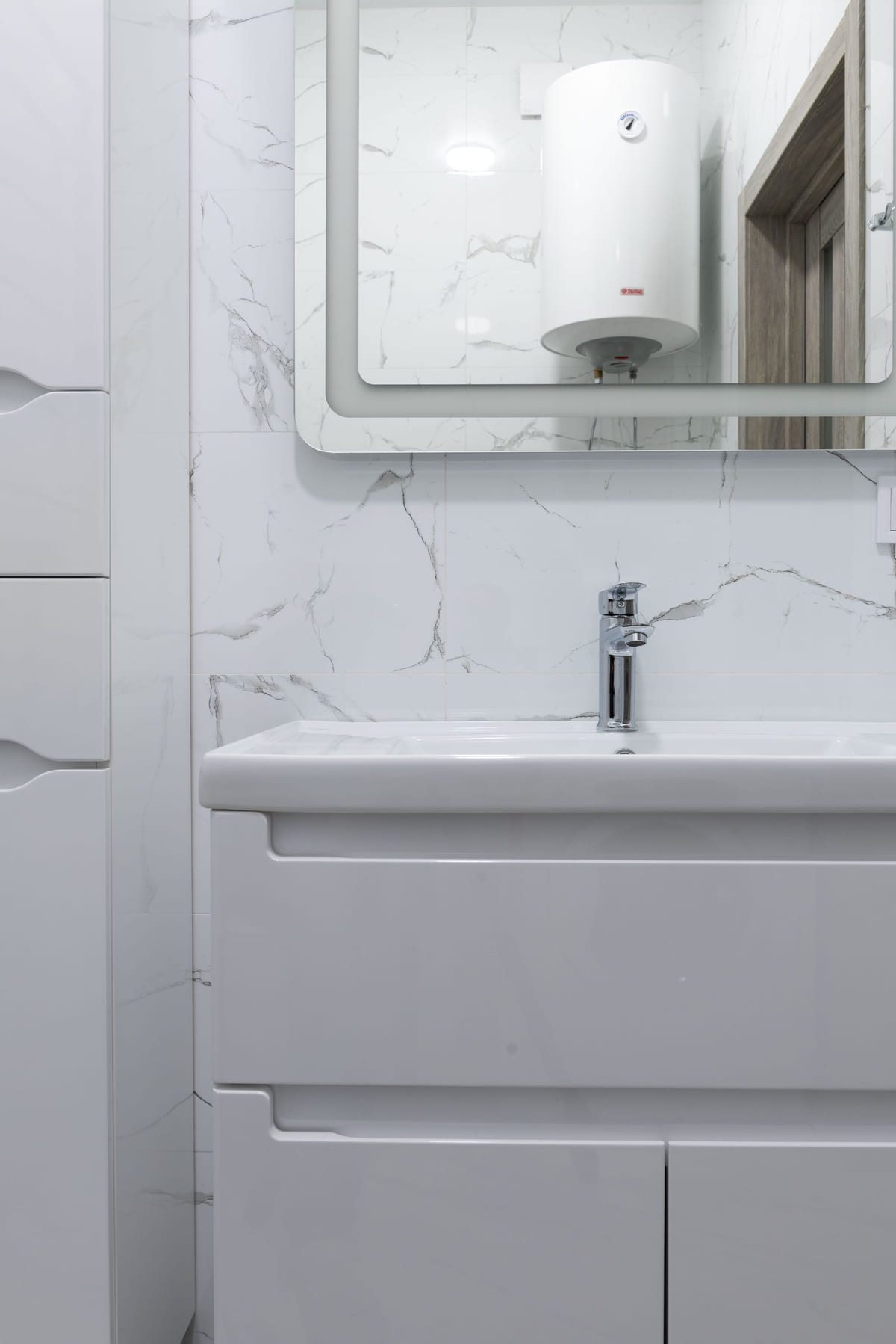 A tank water heater reflected in the mirror of a clean tiled bathroom
