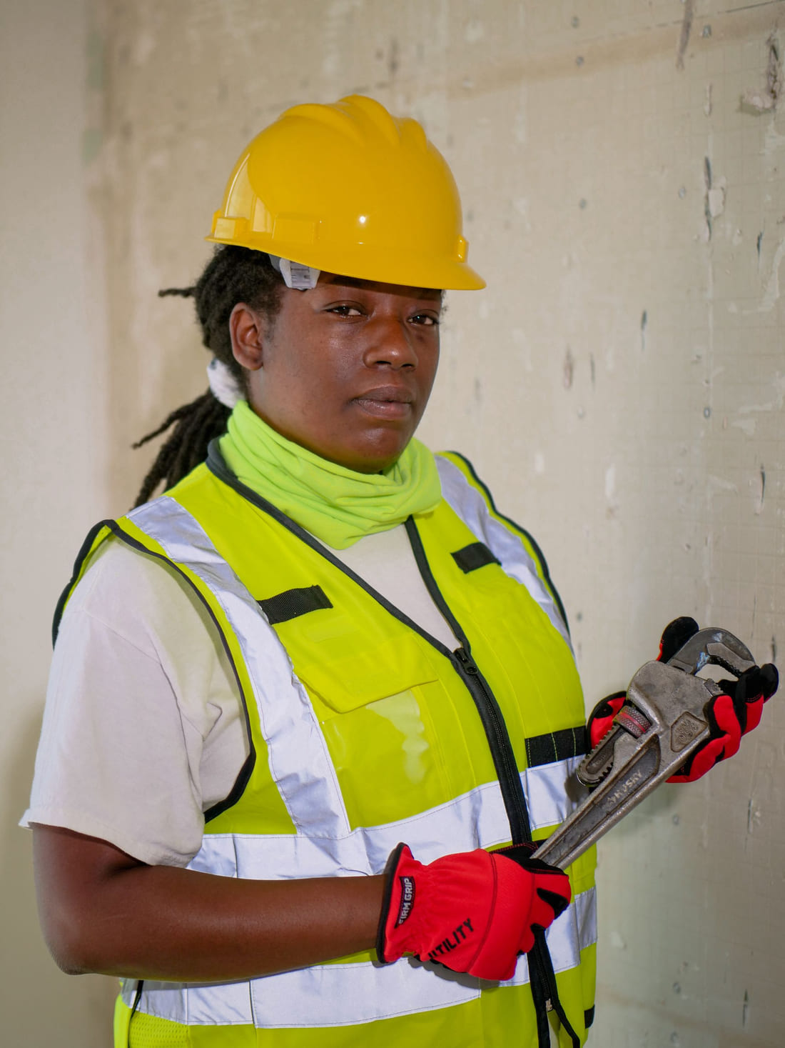A plumber in a high visibility vest holding a pipe wrench