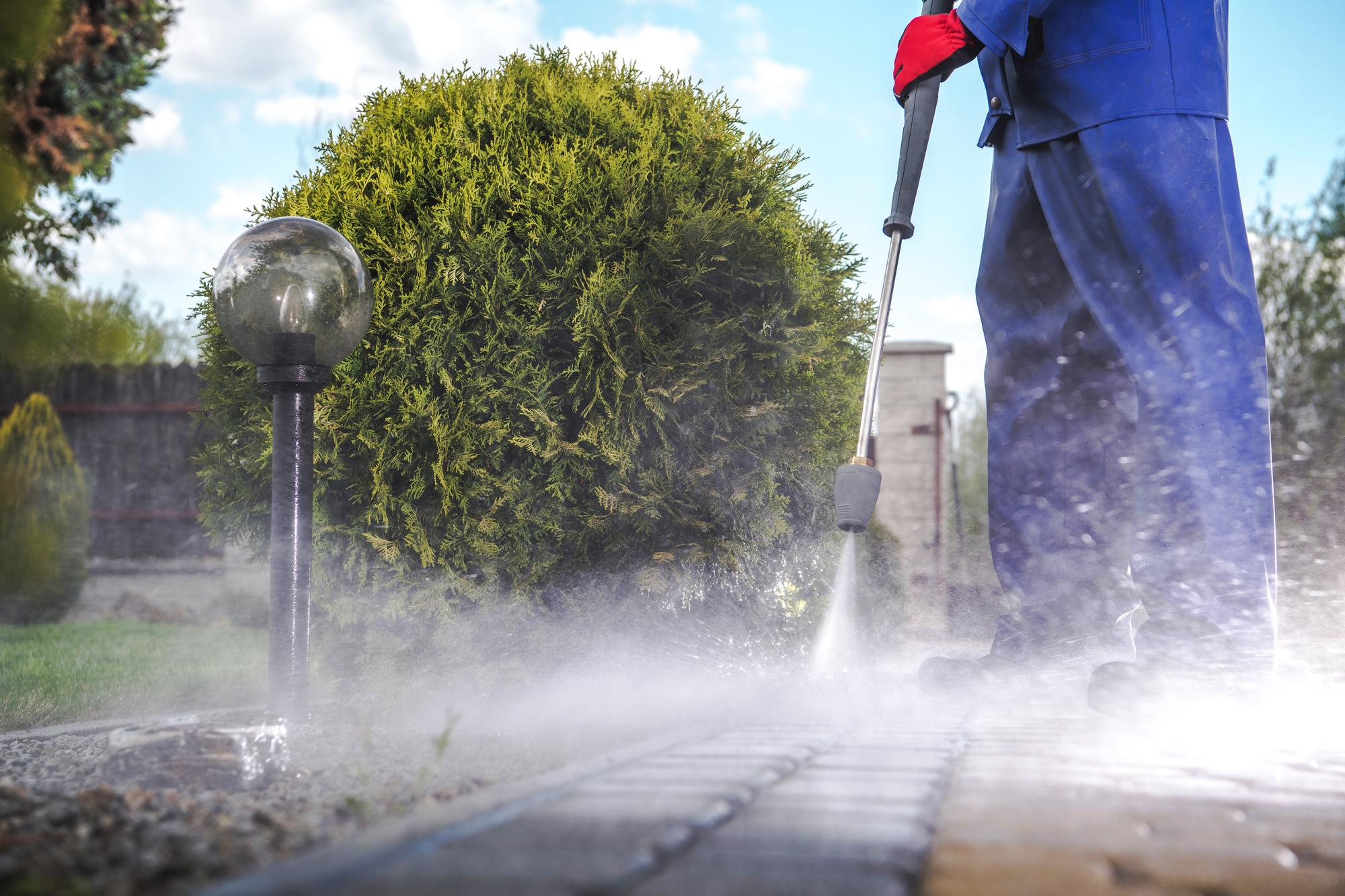 A technician pressure washing a paver walkway on a bright day
