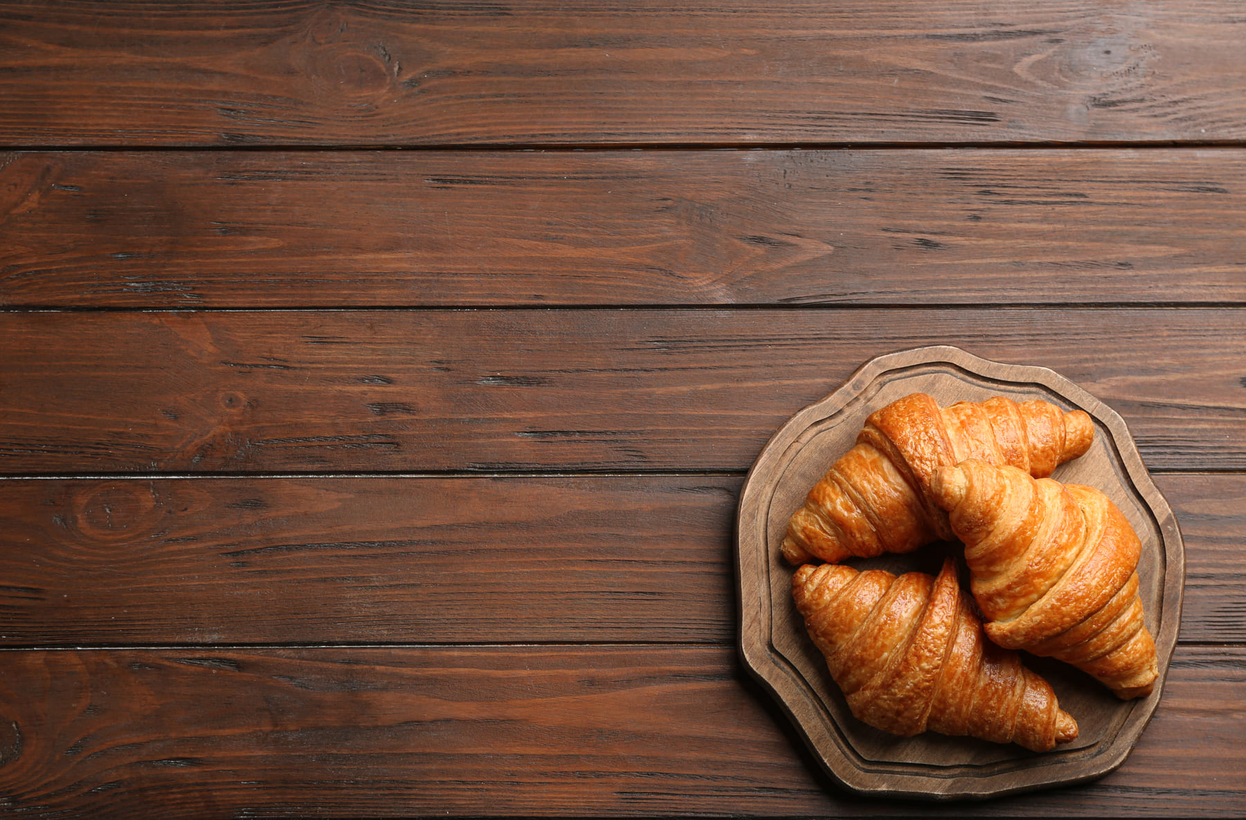 Golden croissants on a wooden board over a dark wood table