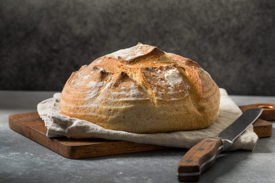 A scored sourdough loaf on a wooden board
